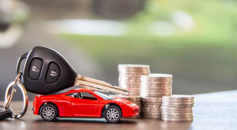 Red toy car with a black car key on top of it in front of three stacks of gold coins