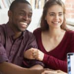 Girl in a maroon shirt smiling with her hands around a man in a purple shirt who is smiling and shaking hands with woman in grey sweater