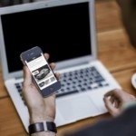 A man looking at his phone in front of a laptop