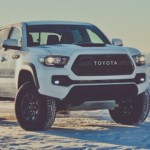 A white Toyota Tacoma atop a snowy mountain with snow-covered trees in back