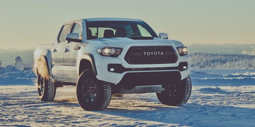 A white Toyota Tacoma atop a snowy mountain with snow-covered trees in back