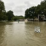 Flooding in a neighborhood, speed limit sign almost completely submerged.