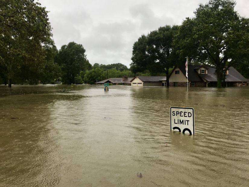 Flooding in a neighborhood, speed limit sign almost completely submerged.