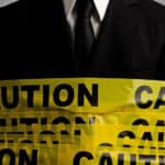 Man in a black suit and white shirt wrapped in yellow caution tape