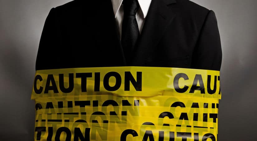 Man in a black suit and white shirt wrapped in yellow caution tape