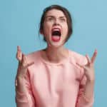 Woman in a pink shirt yelling with her hands up against a blue background