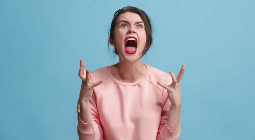 Woman in a pink shirt yelling with her hands up against a blue background