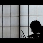 Silhouette of a man on a laptop against a big window