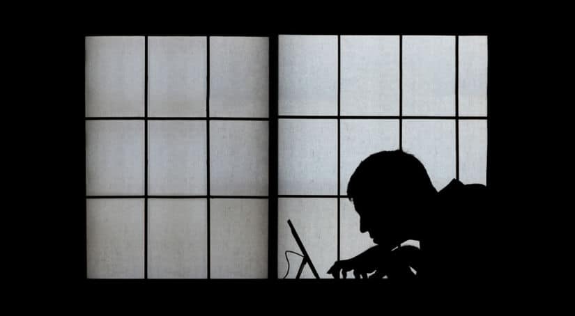 Silhouette of a man on a laptop against a big window