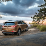 A gold Kia Sportage atop a mountain at a cloudy sunset