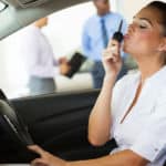 Woman in a white shirt sitting in the driver's seat of a vehicle, kissing a black car key