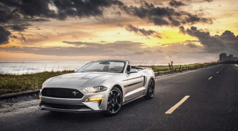 A silver 2019 Ford Mustang convertible with the top down cruises down a sunset lit road