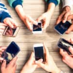 Six pairs of hands in an oval, each pair holding a smartphone