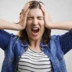 Woman in a black and white stripped shirt and blue denim button up with her hands on her head and her mouth wide open