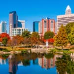Tall buildings with lots of windows behind green and orange trees and a small pond