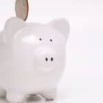 Gold coin going into slot of a white piggy bank with a white background