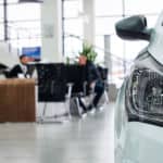 White vehicle's headlight in a large room with two men sitting across from one another at a brown desk in the background