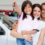 Mom, dad, son, and daughter holding a car key, all smiling standing between two cars