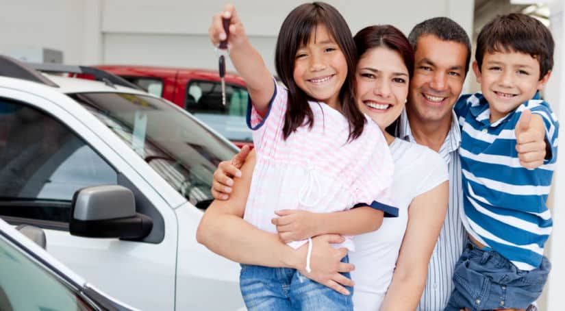 Mom, dad, son, and daughter holding a car key, all smiling standing between two cars