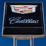 Black, silver, red, gold, and blue Cadillac dealership sign against blue sky