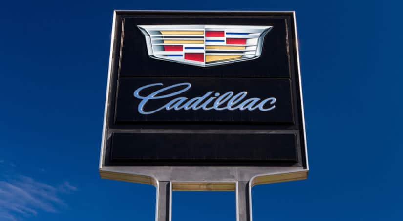 Black, silver, red, gold, and blue Cadillac dealership sign against blue sky