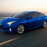 Blue 2018 Toyota Prius driving on highway in front of city skyline