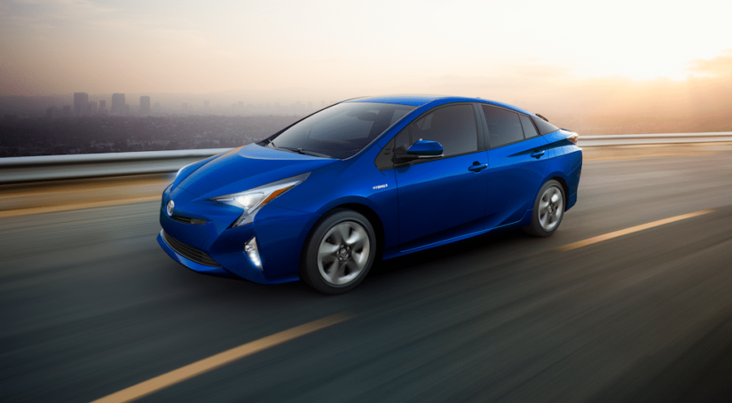 Blue 2018 Toyota Prius driving on highway in front of city skyline