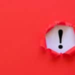 Wall of red paper with a ripped circle in it that reveals a white background and black exclamation point