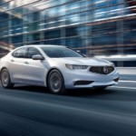 White 2019 Acura TLX driving in front of glass building