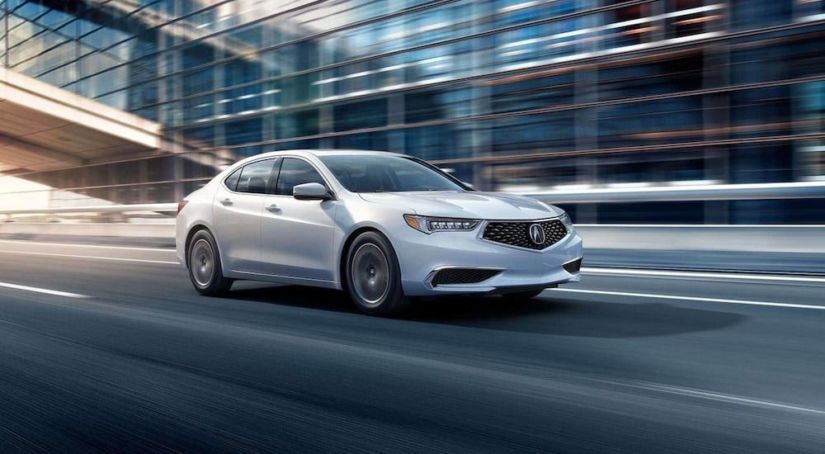 White 2019 Acura TLX driving in front of glass building