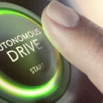 Finger hovering over a circular black button with glowing green edges that says "Autonomous Drive START"