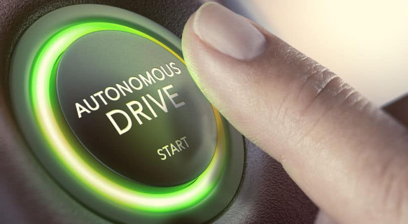 Finger hovering over a circular black button with glowing green edges that says "Autonomous Drive START"