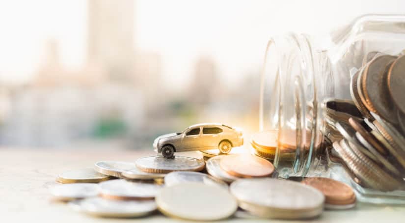 White toy car sitting on top of change that is pouring out of a clear glass mason jar