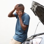 A stressed young man on a cellphone calling for help with his broken down car
