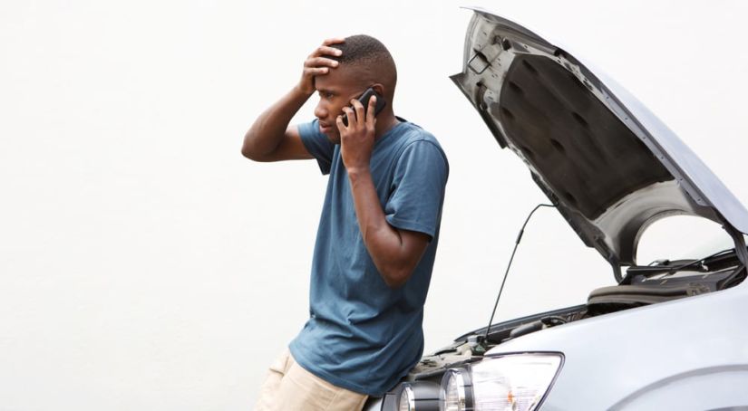 A stressed young man on a cellphone calling for help with his broken down car
