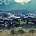 2 blue Chevy trucks sit in front of a mountain range