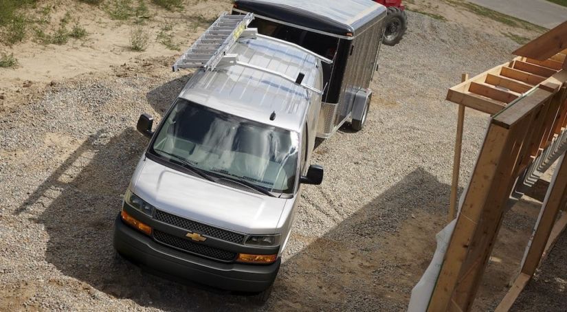 Silver 2018 Chevy van with ladder on roof and towing trailer
