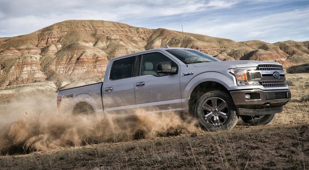Silver 2019 Ford F150 driving on dirt road with mountains in back
