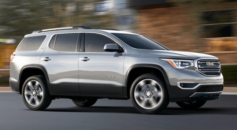 Silver 2019 GMC Acadia driving on out of focus city street