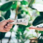 One hand giving a stack of cash to another hand holding a toy car