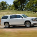 White 2019 Chevrolet Suburban driving in front of hilly field