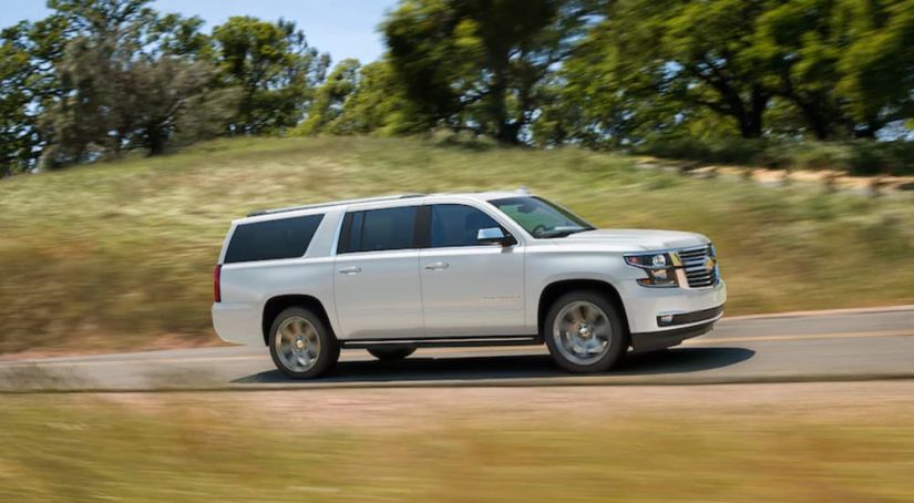 White 2019 Chevrolet Suburban driving in front of hilly field
