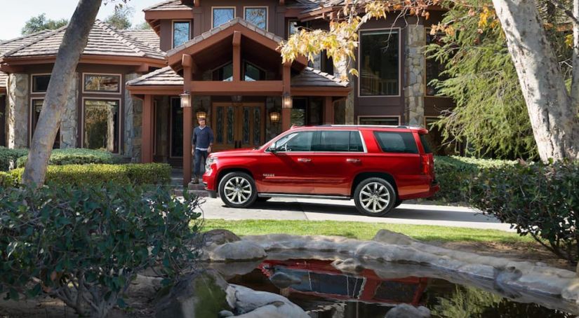Man walking towards red 2019 Chevy Tahoe in front of mansion