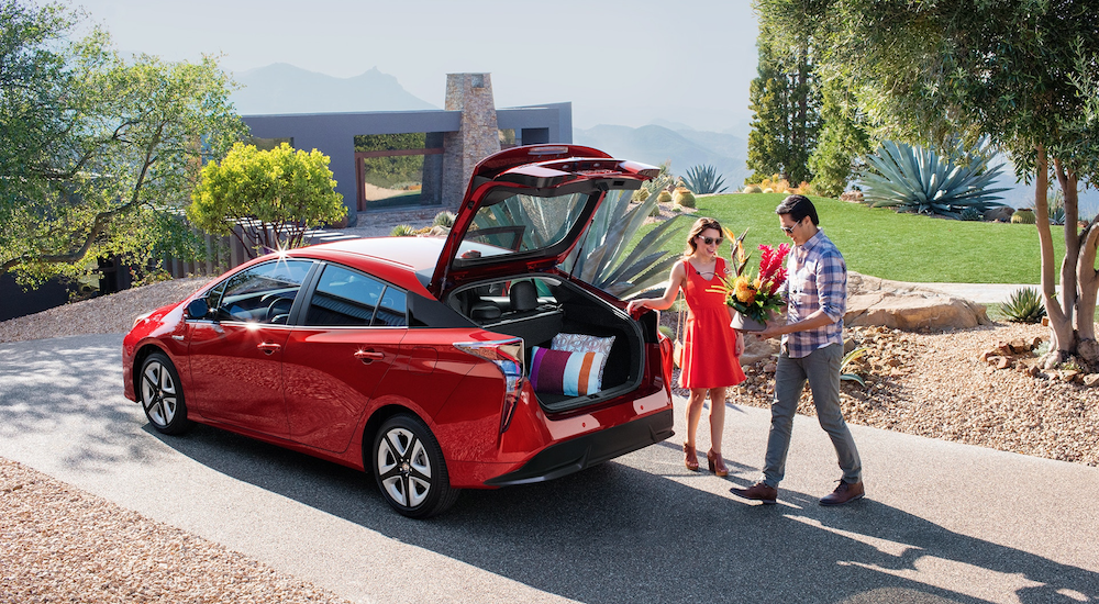 Man and woman loading tropical plants into red 2019 Toyota Prius in front of mountaintop home