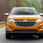 An orange 2019 Chevy Equinox driving on a winding woodland road towards the camera