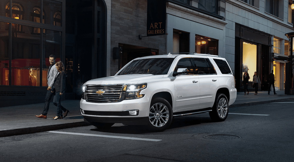 A man and woman walk away from a white 2019 Chevy Tahoe on a busy city street