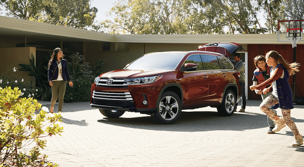 A dark red 2019 Toyota Highlander in a yard with a family around it