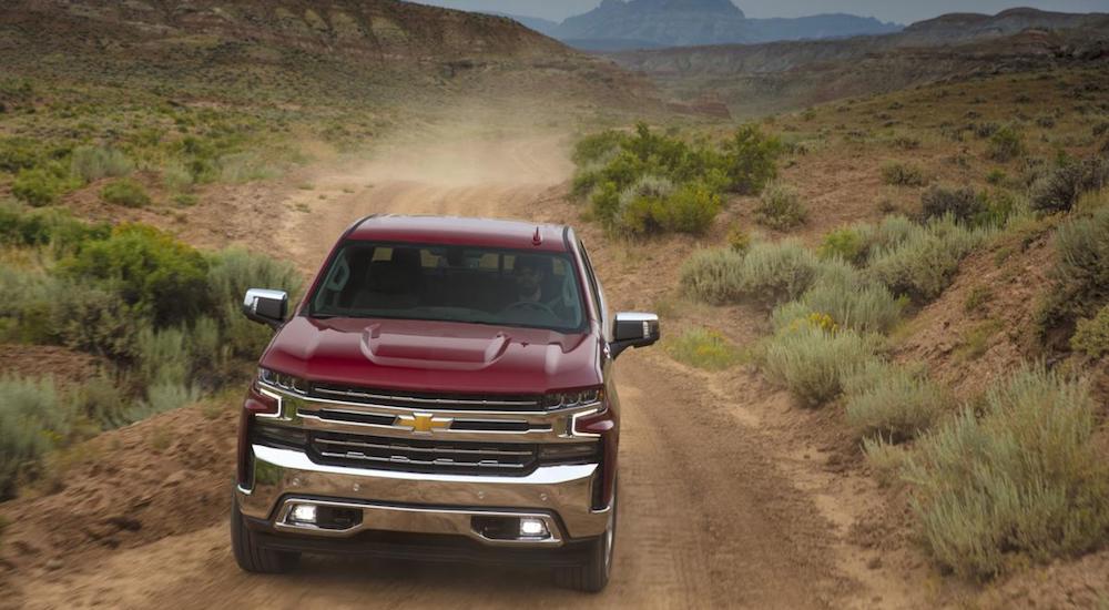 A red 2019 Chevy truck for sale travels a dusty dirt road in a desert