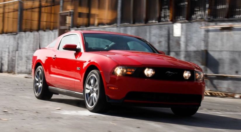 A red 2015 Ford Mustang drives past an industrial building