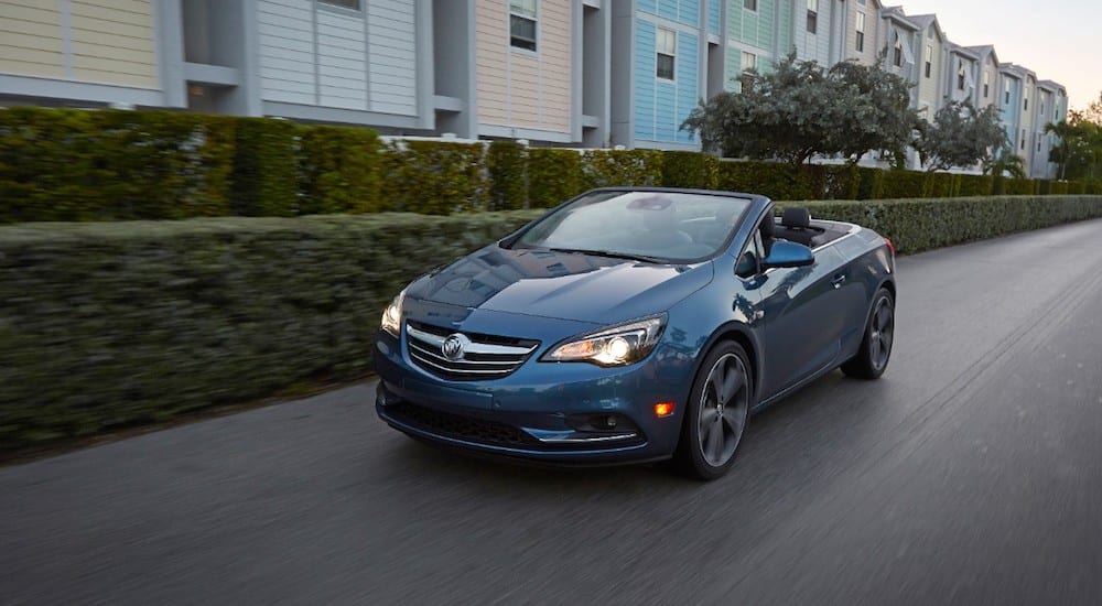 A blue 2019 Buick Cascada Convertible driving by multi-colored houses